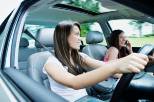 Two teenage girls (12-16) driving in car, one girl with mobile phone